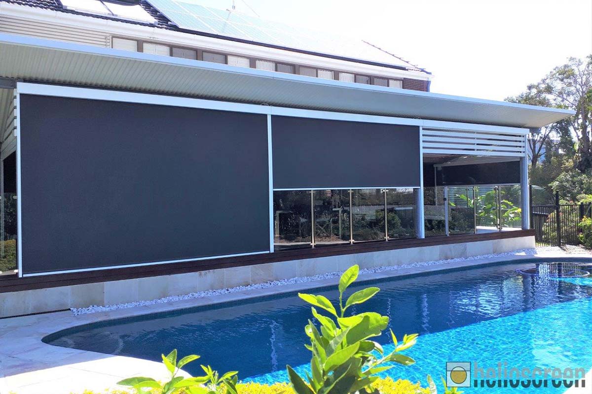 Three charcoal zip-track outdoor blinds fully lowered across a pergola-covered deck beside a swimming pool, with solar panels visible on the roof behind.