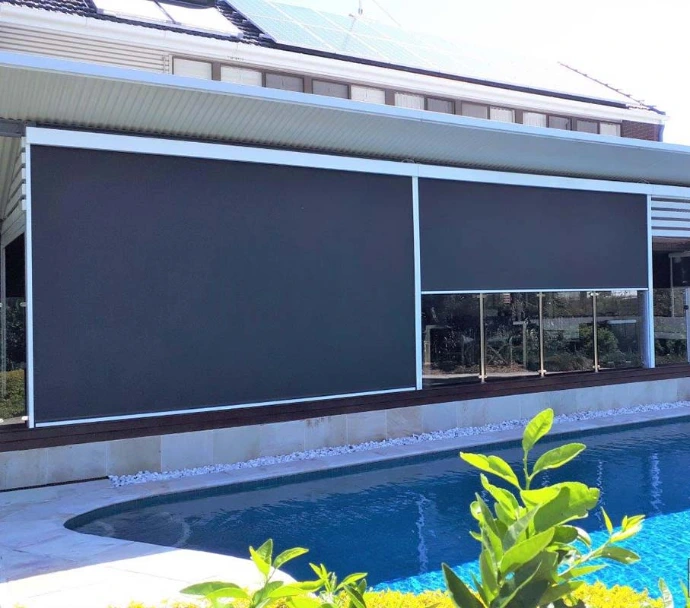 Two large charcoal zip-track outdoor blinds fully lowered across a pergola-covered deck beside a swimming pool, with glass pool fencing and solar panels visible on the roof behind.